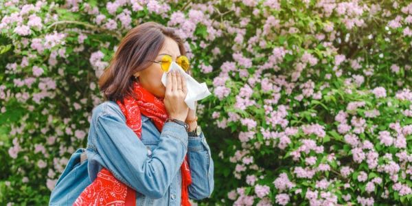 Allergy concept. Young asian woman sneezes and blowing her nose with a handkerchief and suffering in the spring among flowering and blooming trees.