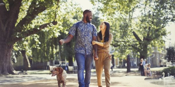 Happy young couple walking dog in sunny park