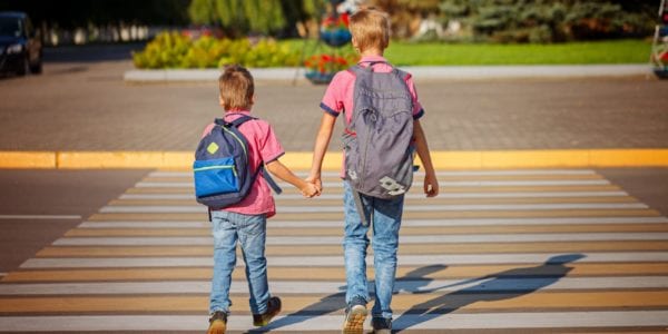 Two brothers with backpacks walking across the street
