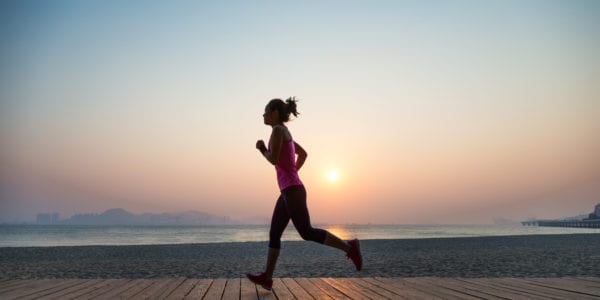 Silhouette of young woman jogging on shore at sunrise.