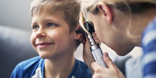 Little boy having a medical ear examination. The smiling boy is aged 7. The doctor is vising boy at home and using otoscope to examine the boy's ear.