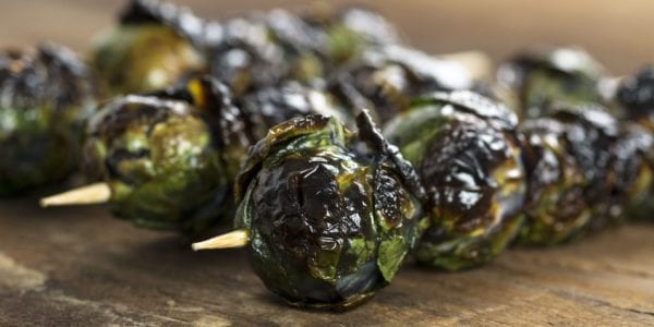 Three grilled organic purple Brussels sprouts on skewers set on wood