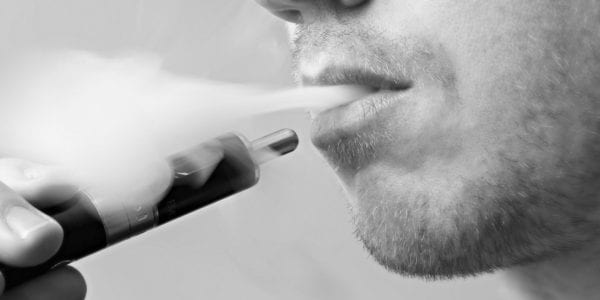 a closeup of a mans mouth as he exhales smoke.