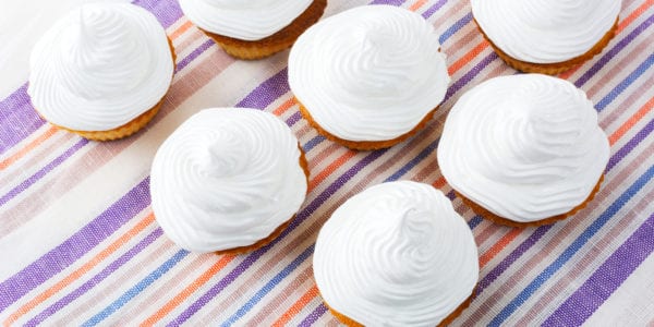 White cupcakes on the striped linen napkin top view. Sweet gourmet pastry dessert. Homemade cupcakes with whipped cream.