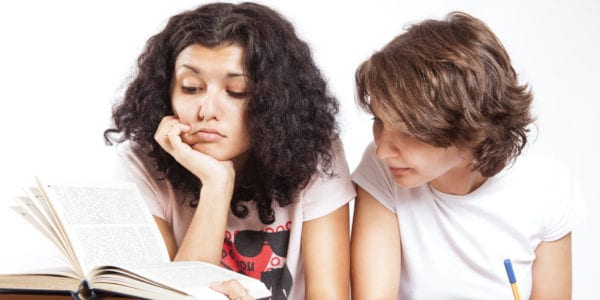 Two college-aged girls studying a stack of books.