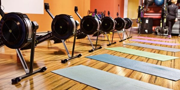 Yoga mats are stretched out in front of rowing machines in a gym studio.