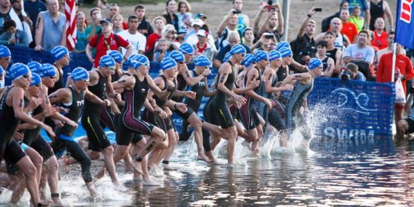 Image of the start of a triathlon, with female competitors running into the water.