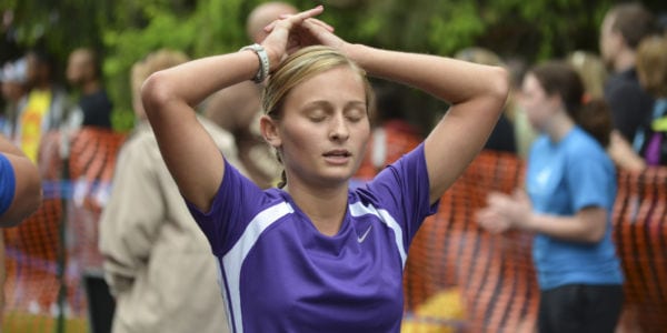 Picture of a female runner with eyes closed and hands on top of her head.
