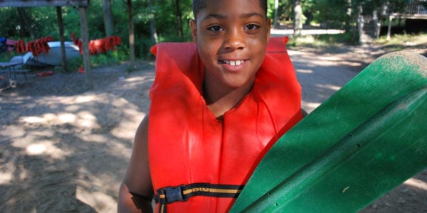 Image of a boy camper holding a paddle and wearing a life vest