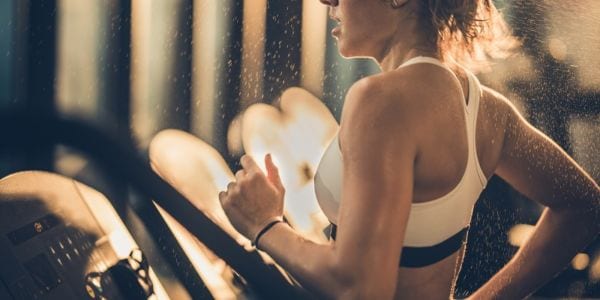 Sweaty woman running on treadmill during sports training in a gym.