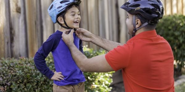 Image of a dad helping his son put on a bike helmet.