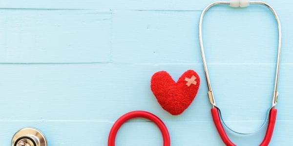 Image of felt heart with bandage on it, red stethoscope on blue background.