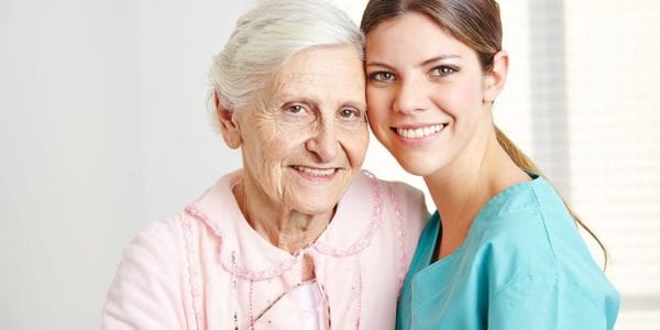 Smiling female caregiver embracing happy senior woman in nursing home