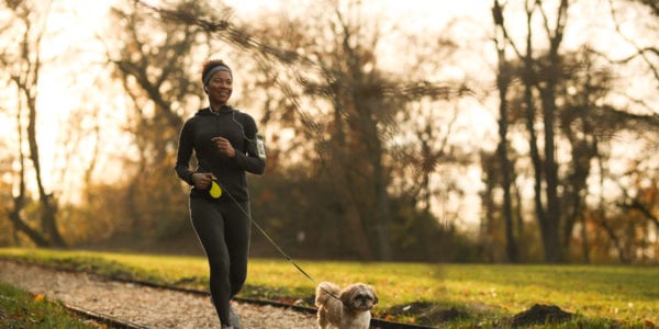 Happy black sportswoman running with her dog at the park.