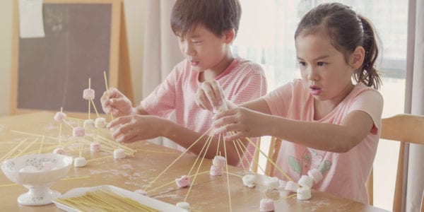 Mixed race young Asian children building tower with spaghetti and marshmallow learning remotely at home, STEM science, homeschooling education, Social distancing, isolation concept