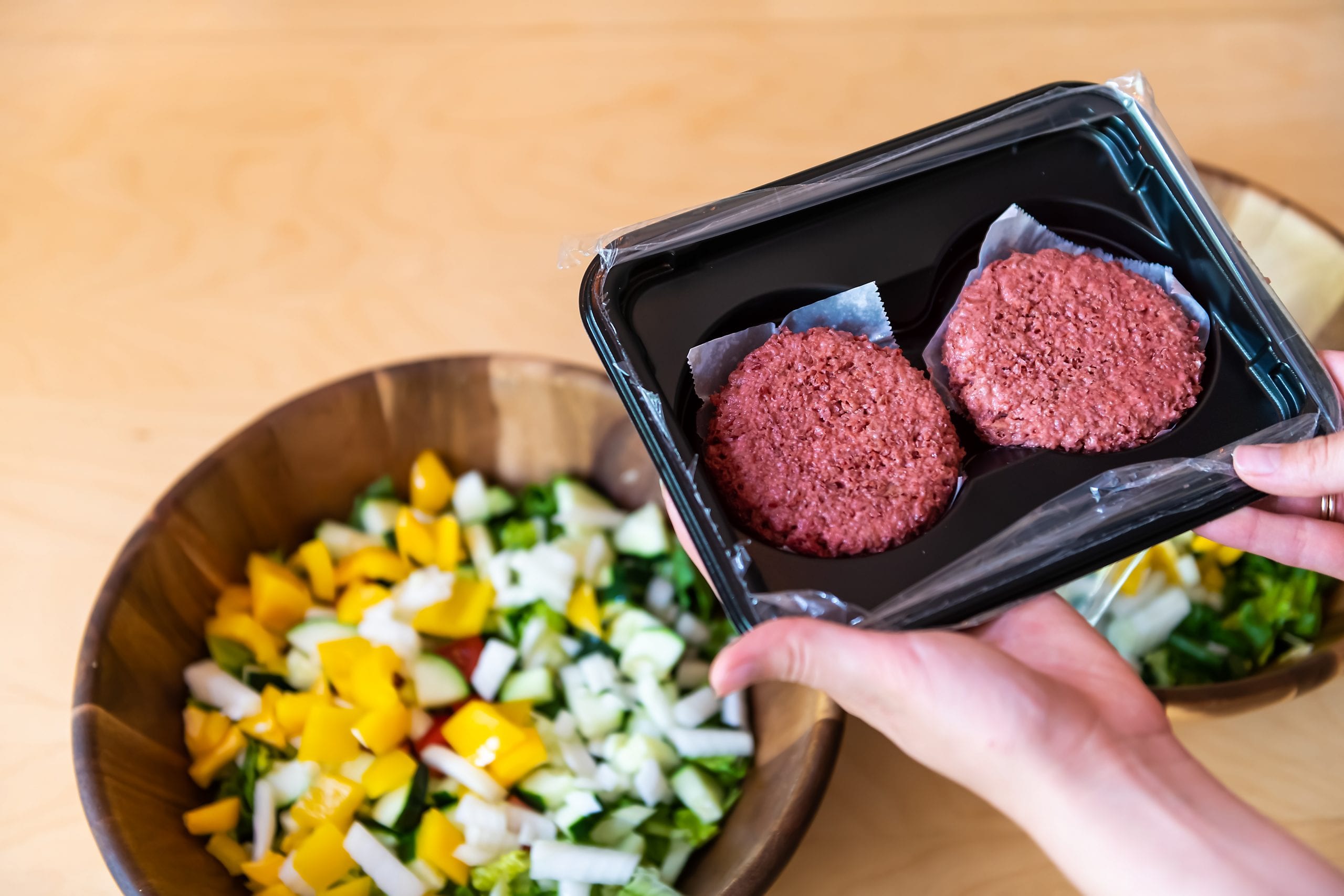 Woman holding two raw uncooked red vegan meat burger patties by salad bowls in packaging