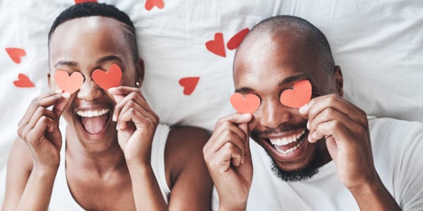 Shot of a happy young couple playing with cut out red hearts in bed at home