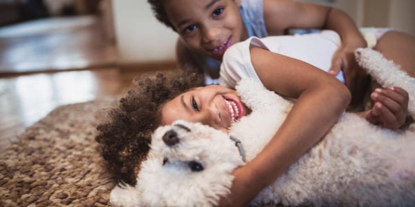 Cute mixed - race siblings having fun, playing at home with dog