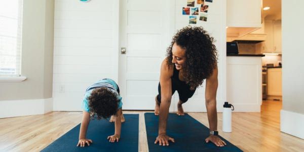 A mother exercises with her young son inside their home. She is teaching the boy the importance of a healthy lifestyle by proper stretching and exercising.