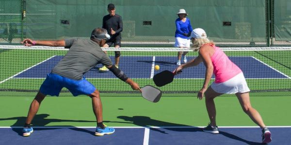 Two couples play pickleball on an outdoor court.