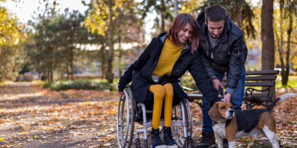 Disabled girl with boyfriend playing with dog in the park in autumn