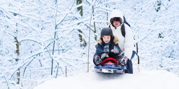 Little boy sledding down hill with his father helping him