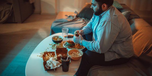 Large man with binge eating disorder eating junk food in living room