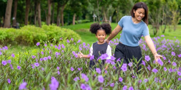 Happy mixed race family mother with little daughter holding hands and walking together in the garden. Smiling mom with cute child girl enjoy and having fun in summer outdoor weekend holiday vacation
