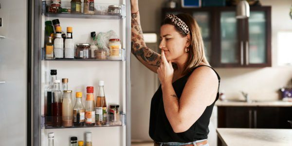 Young woman looks into the fridge wondering why am I hungry all the time