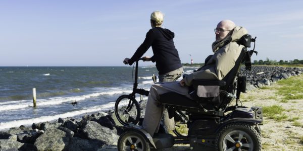 a handicapped man at the beach. electric wheelchair. with assistant on bicycle.