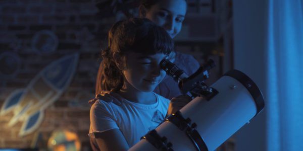 Cute sisters watching the stars together at home using a telescope, family and leisure concept