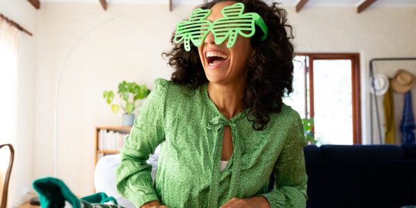 Caucasian woman dressed in green with shamrock glasses for st patrick's day laughing