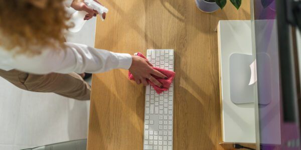Woman wipes down her keyboard at her work station while spring cleaning