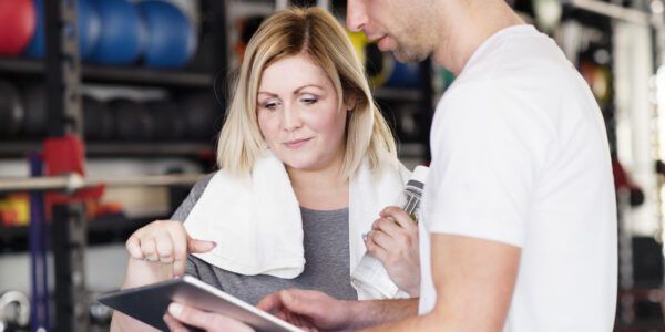 A woman at the gym has a discussion with a personal trainer.