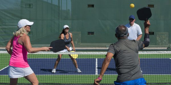A group of men and women play pickleball outside.